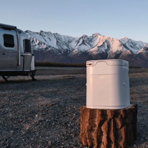 Ogo Composting Toilet on a stump next to a camper in front of a snow covered mountain